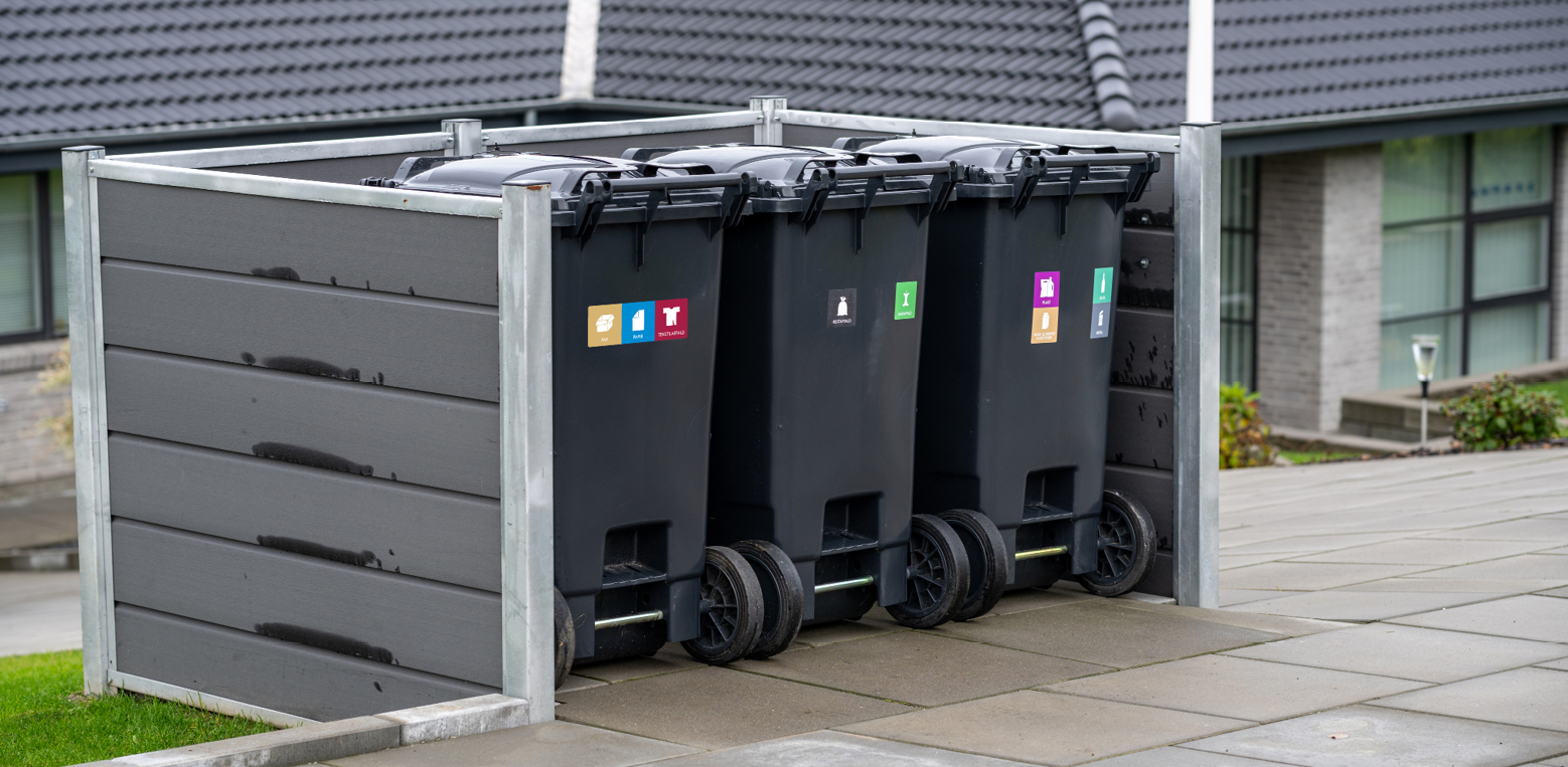 De nye affaldsbeholdere placeret i et beholderskjul. Her med de nye piktogrammer.